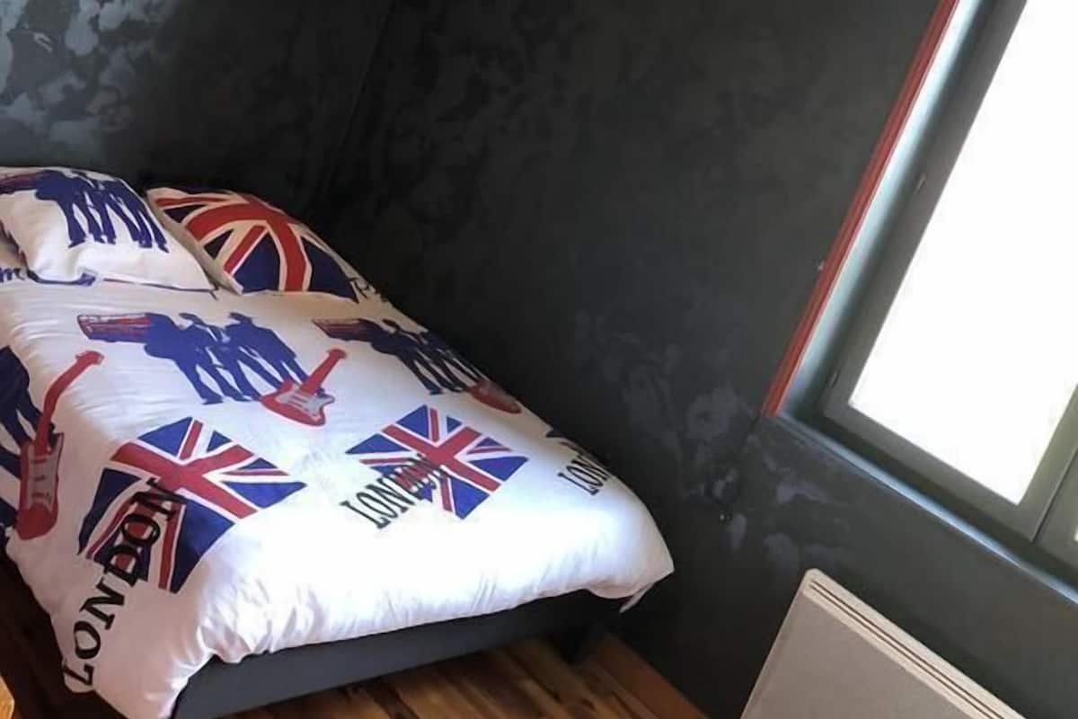 A bedroom with a bed, dark walls, a window, and a wooden floor.