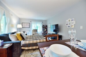 Ein Wohnzimmer mit einer Couch, einem Esstisch gedeckt mit Tellern und einem Weinglas sowie einem gemusterten Teppich.