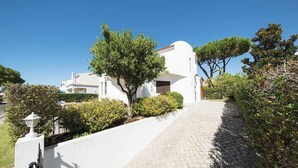 Une villa blanche avec une allée pavée et une entrée fermée par un portail.
