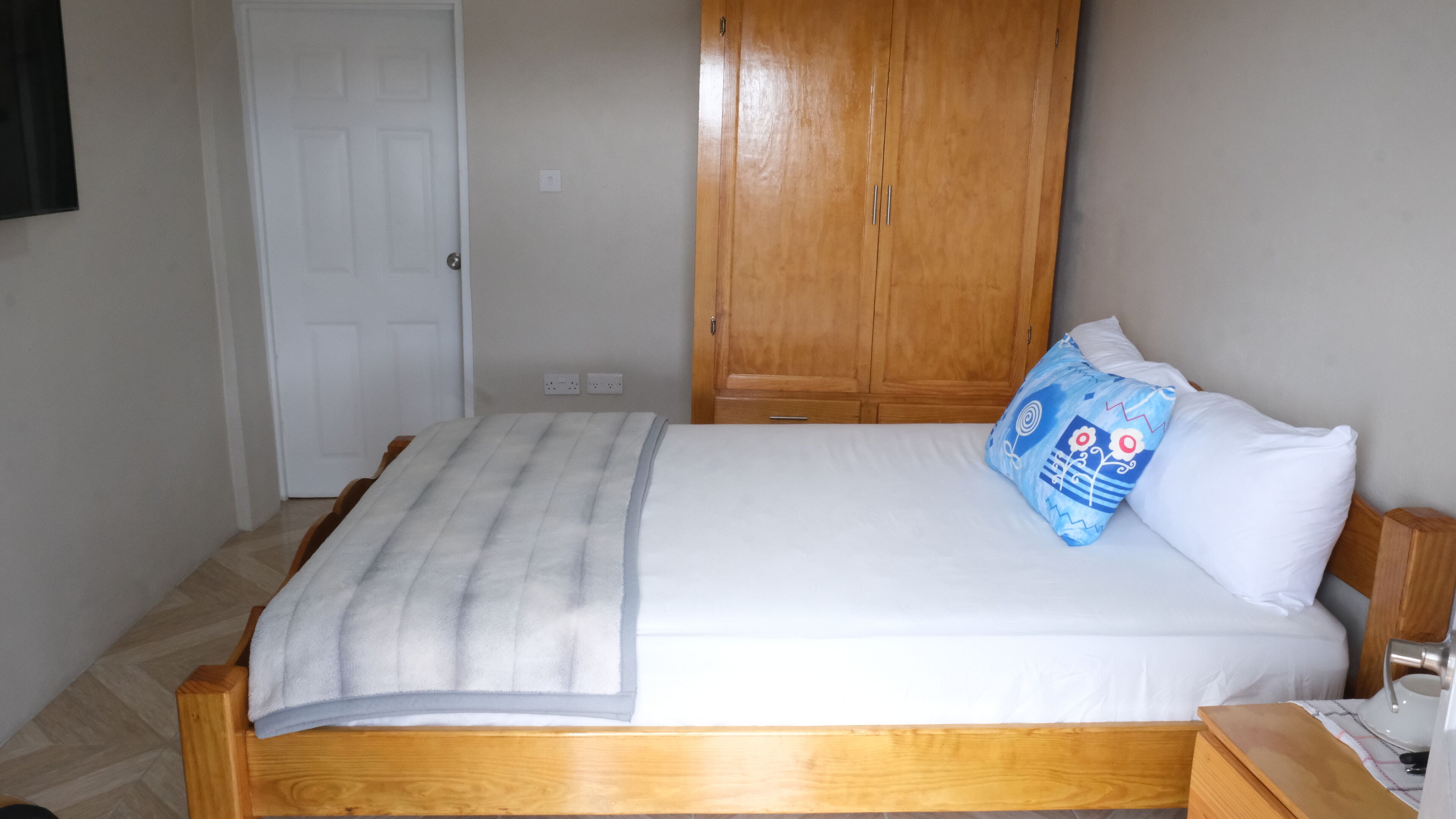 Un dormitorio con cama de madera, ropa de cama blanca, almohada azul y un armario de madera.