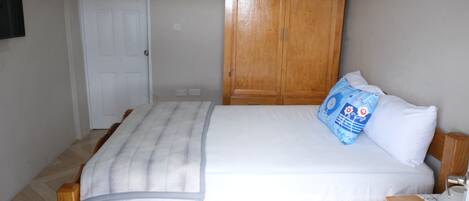 A bedroom with a wooden bed, white bedding, a blue pillow, and a wooden wardrobe.