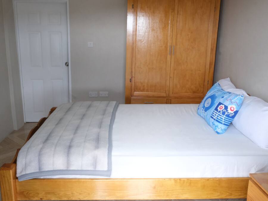 A bedroom with a wooden bed, white bedding, a blue pillow, and a wooden wardrobe.