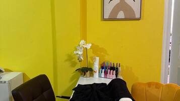 A room with a yellow wall, a white table, a black chair, a yellow chair, and a framed artwork.