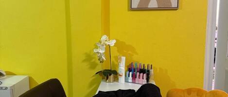 Una habitación con una pared amarilla, una mesa blanca, una silla negra y una silla amarilla, además de una obra de arte enmarcada.