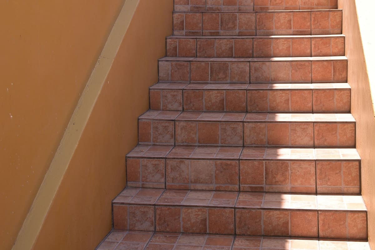 A set of outdoor stairs with a yellow wall on one side and a white railing on the other.