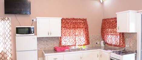A compact kitchen with white cabinets, a microwave, a stove, and a sink.