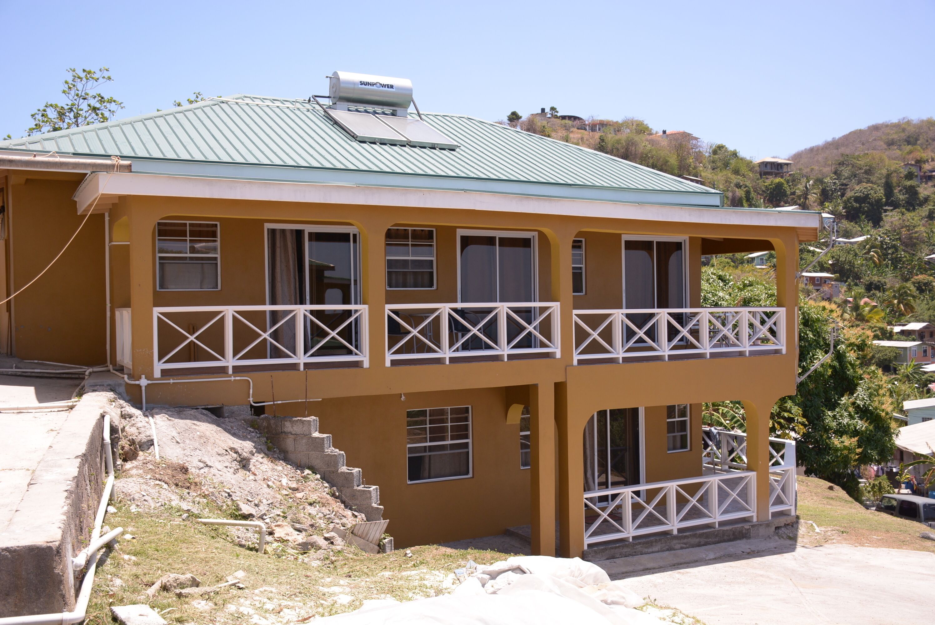 A two-story building with a green roof, multiple balconies, and a staircase leading to the upper level.