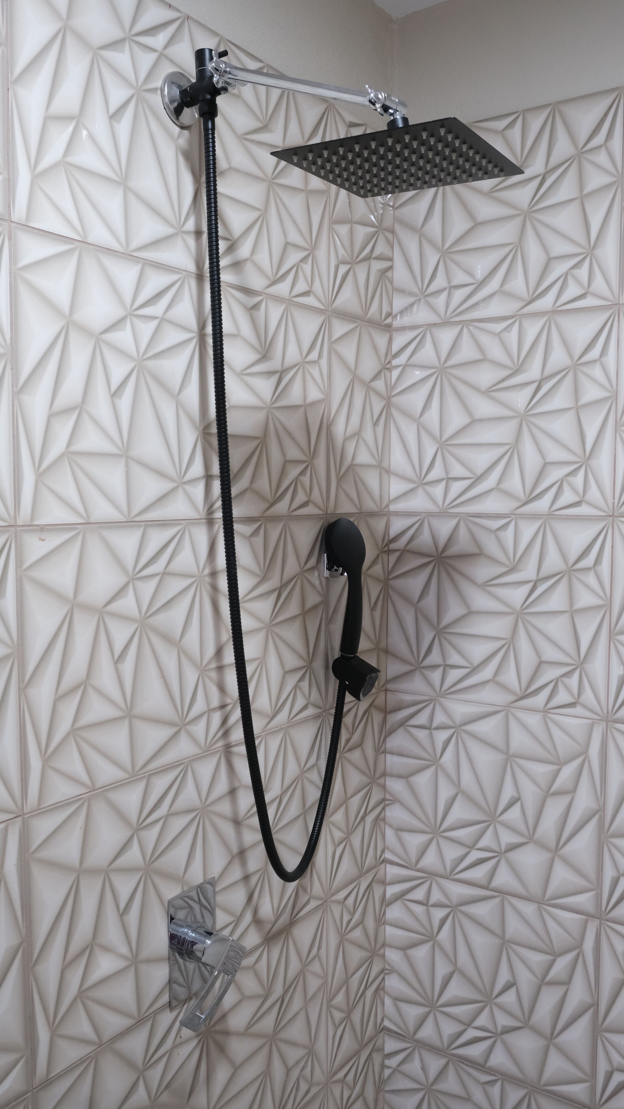 A shower with a geometric tile pattern on the wall and a handheld showerhead.