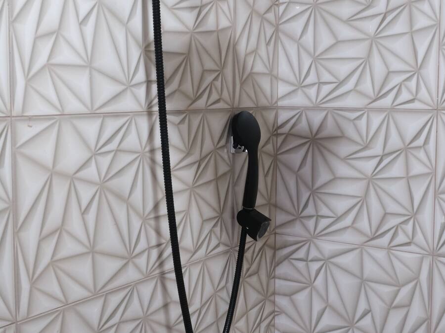A shower with a geometric tile pattern on the wall and a handheld showerhead.