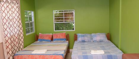 Quarto com duas camas de madeira, uma janela, cortina e uma mesa.