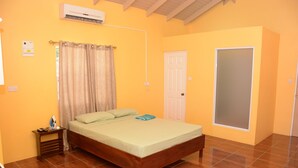 Un dormitorio con una cama de madera, una mesita de noche, una cortina, una puerta y un equipo de aire acondicionado.