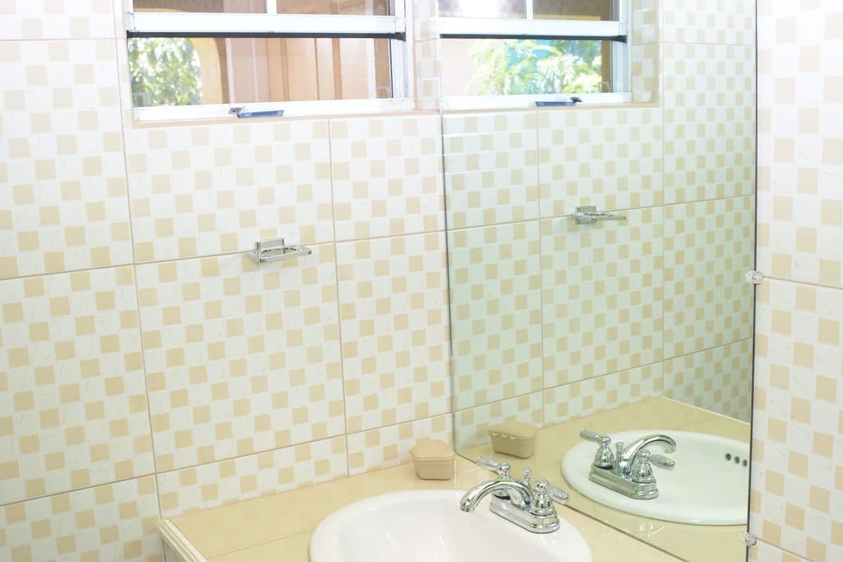 A bathroom with a checkered tile wall, a sink with a mirror, and a window above the sink.