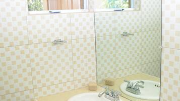 Un bagno con parete rivestita di piastrelle a scacchi, un lavabo con specchio e una finestra sopra il lavabo.