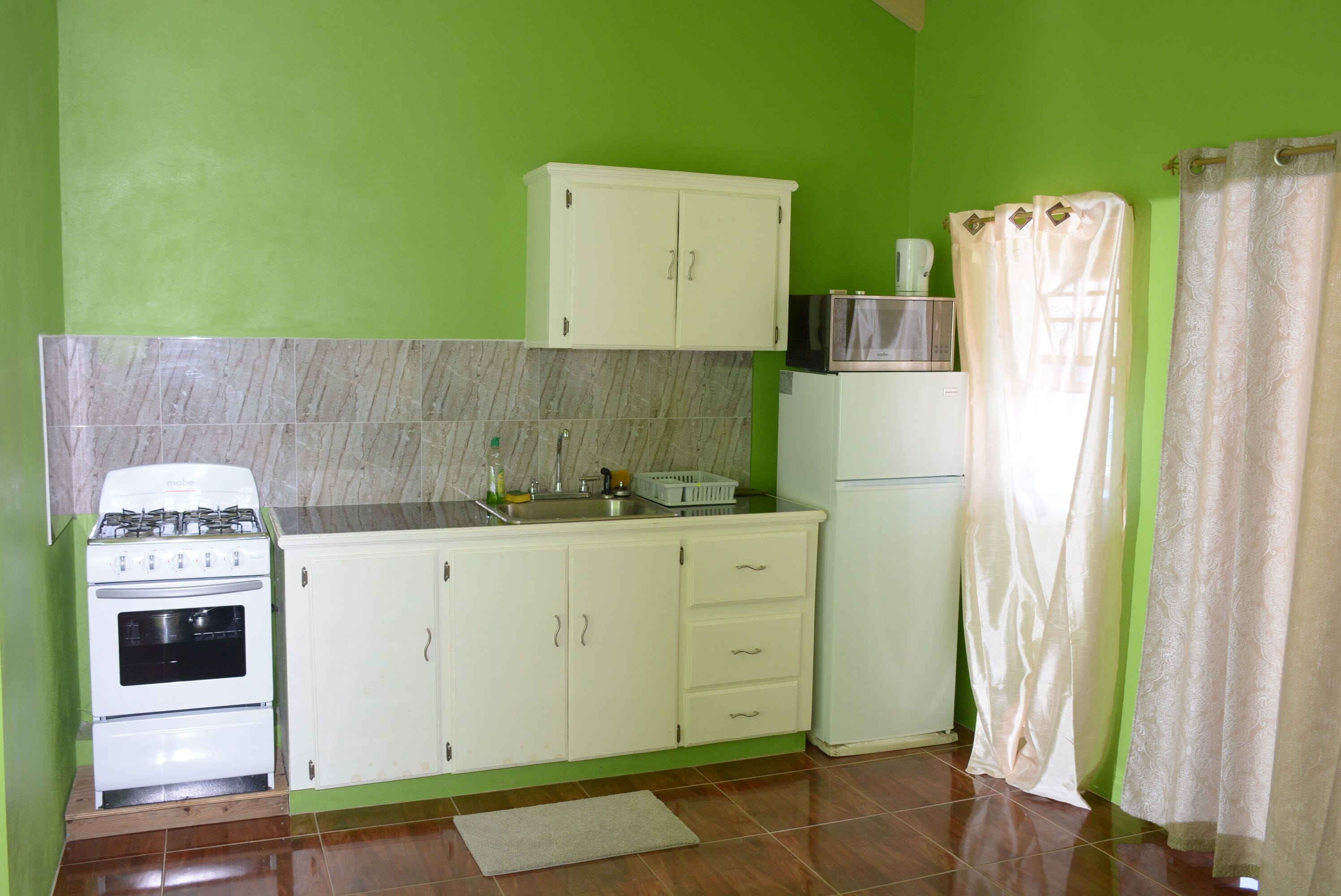 A compact kitchen with white cabinets, a stove, a microwave, and a refrigerator.