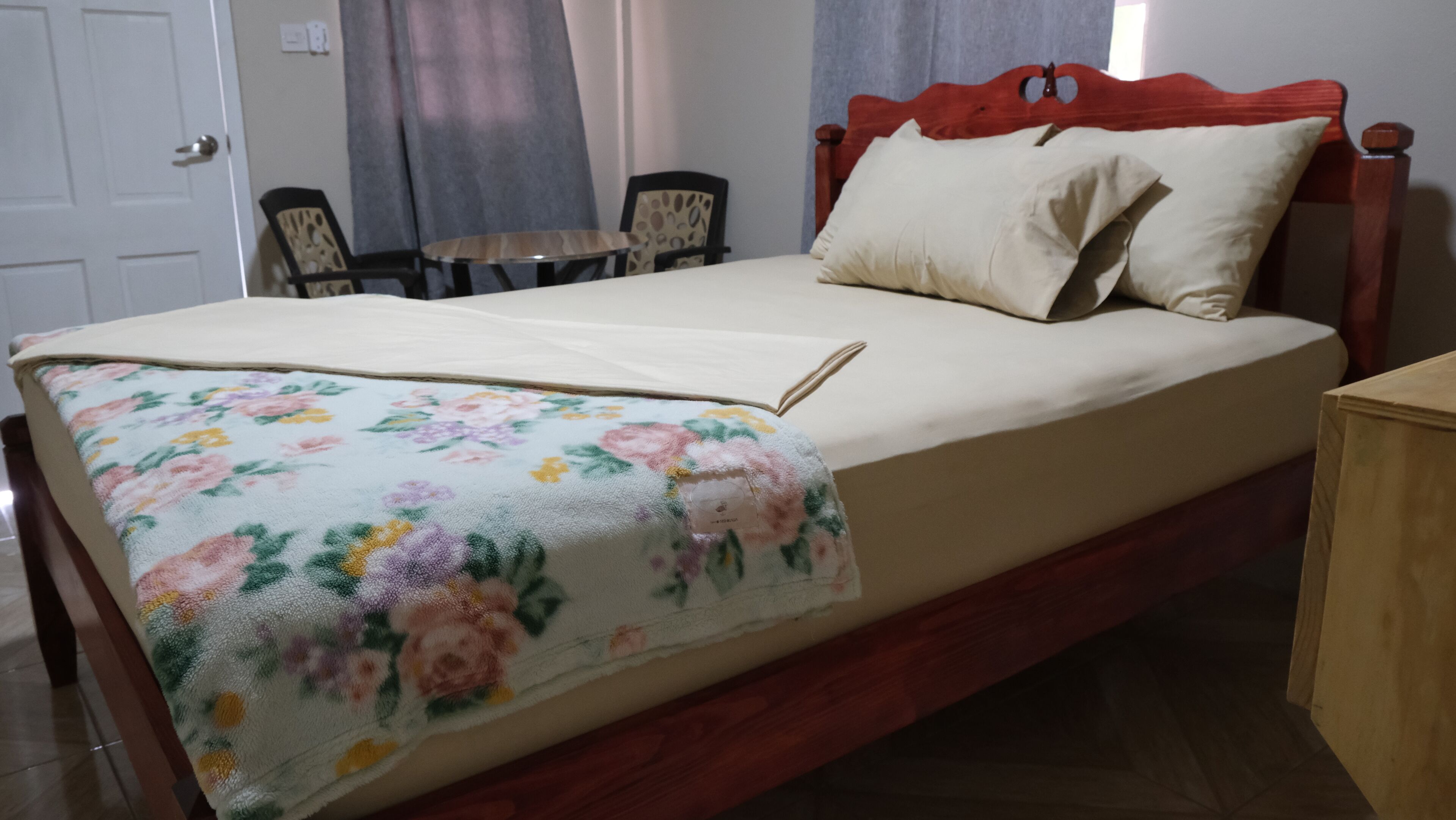 Een bed met een bloemenbedekking, een houten hoofdbord en een nachtkastje.