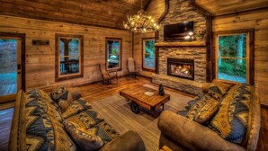 A log cabin interior with a stone fireplace, wooden walls, and a chandelier. - Sleepy Bear Hideaway - Close to Train, Mountain Views, Hot Tub (Blue Ridge)