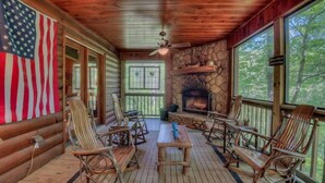A log cabin with a stone fireplace, wooden chairs, and a large American flag. - Riverwalk- to Toccoa River | Screened Porch | Pet Friendly | Fenced Yard (Blue Ridge)