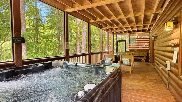 A cabin with a hot tub, wooden deck, and large windows overlooking a forest. - Riverwalk- to Toccoa River | Screened Porch | Pet Friendly | Fenced Yard (Blue Ridge)