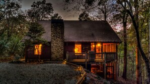A rustic log cabin with a stone chimney, a wooden deck, and a porch with a railing. - Riverwalk- to Toccoa River | Screened Porch | Pet Friendly | Fenced Yard (Blue Ridge)