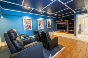 Ein Heimkino mit blauen Wänden, schwarzen Ledersesseln und Holzboden.