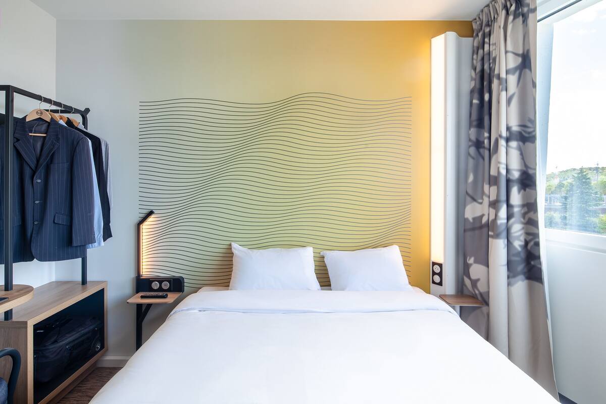 A hotel room with a bed, bedside tables, a wardrobe, and a view of the outdoors.