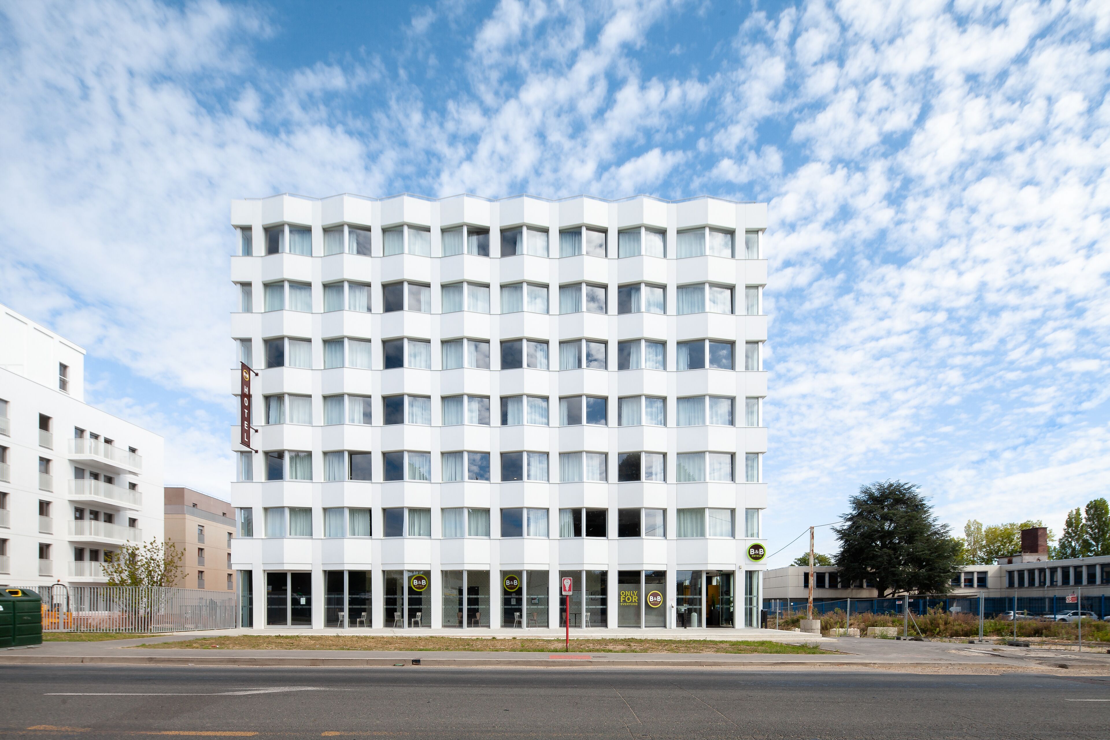 A modern hotel with a grid of windows and balconies, a visible sign for the hotel, and a clear sky.