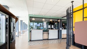 A modern hotel lobby with a reception desk, seating area, and a coffee machine. - B&B HOTEL MASSY Gare TGV (Massy)