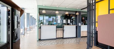 Un moderno vestíbulo de hotel con mostrador de recepción, zona de estar y una máquina de café.