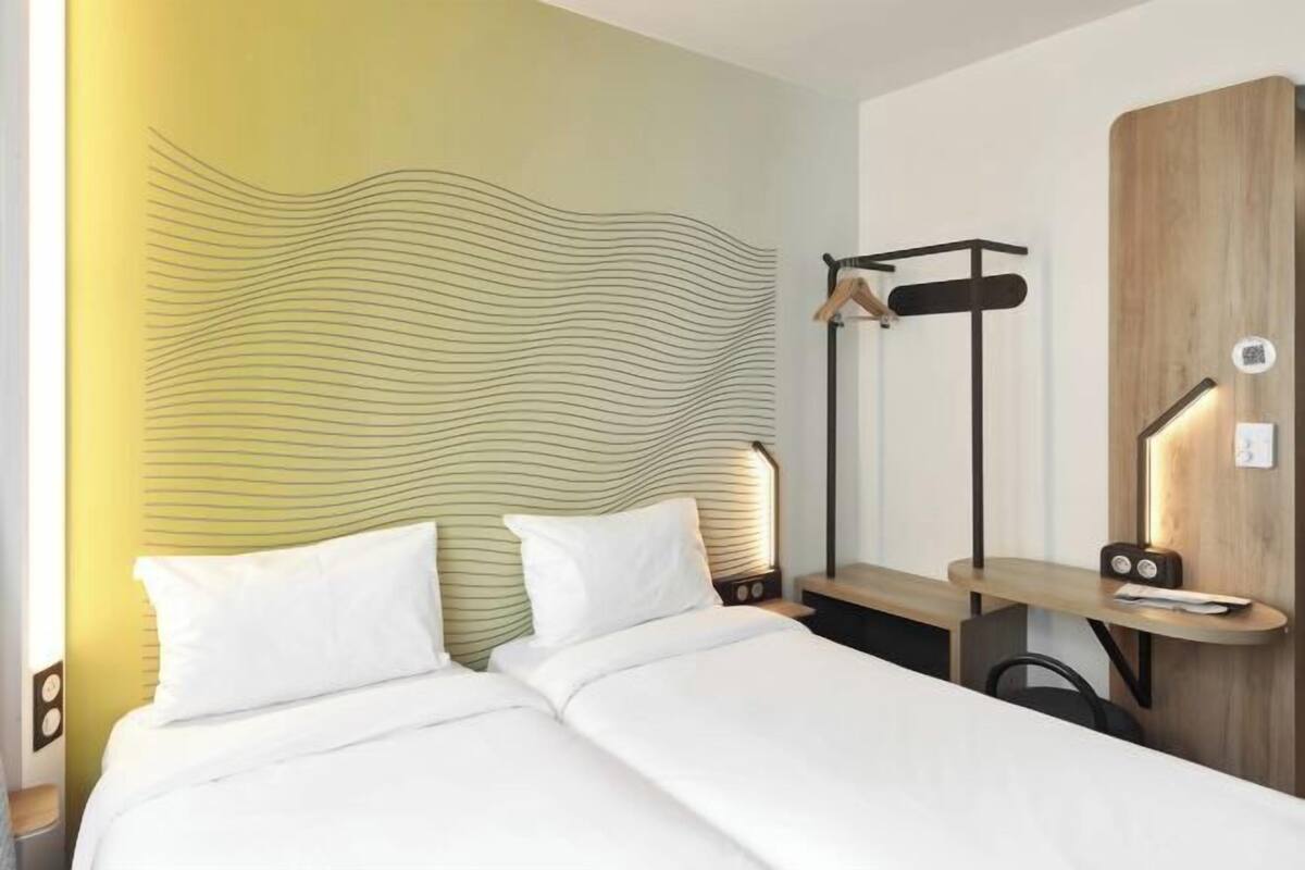 A hotel room with a bed, bedside table, lamp, and a wall with a wavy pattern.