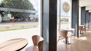 A modern hotel interior with large windows, a view of the street, and a logo on the wall. - B&B HOTEL MASSY Gare TGV (Massy)