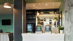 A bar area with a counter, shelves with glasses and bottles, and a television on the wall. - B&B HOTEL MASSY Gare TGV (Massy)