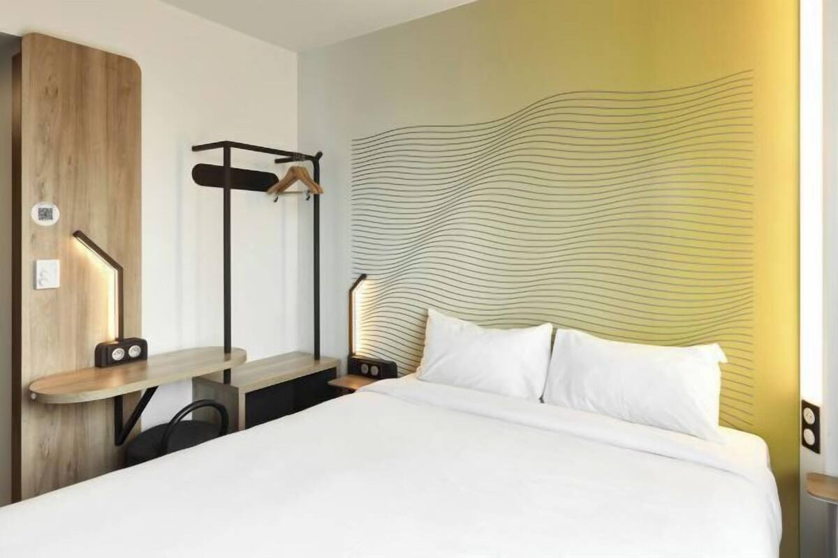 A hotel room with a bed, bedside table, lamp, and a wall with a wavy pattern.