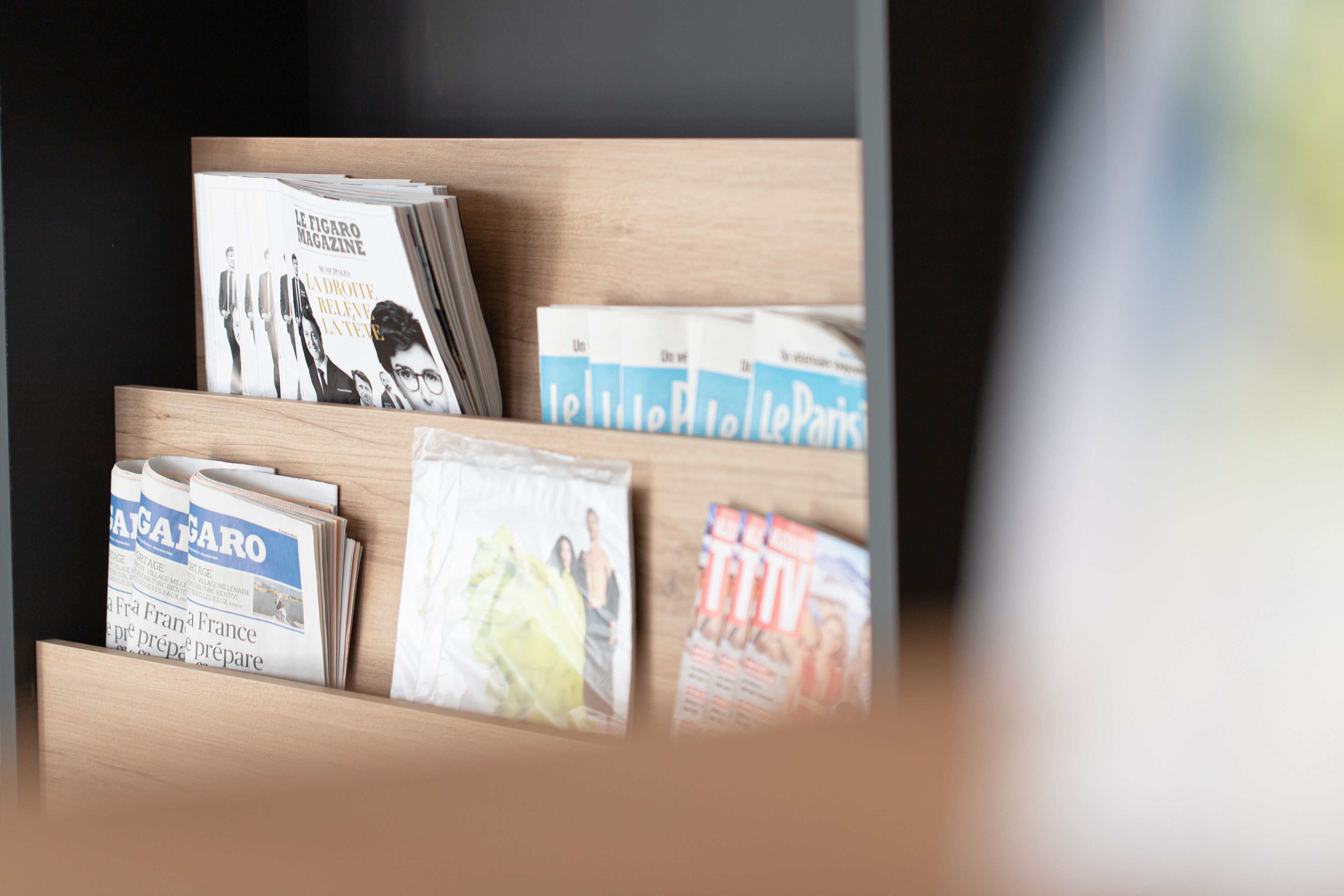 Ein hölzerner Zeitschriftenständer mit verschiedenen Zeitschriften, darunter 'Le Figaro' und 'Le Parisien'.