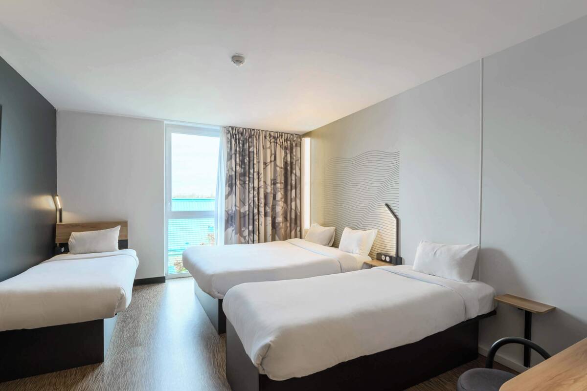 A hotel room with two beds, a desk, a chair, a lamp, and a view of the sea.