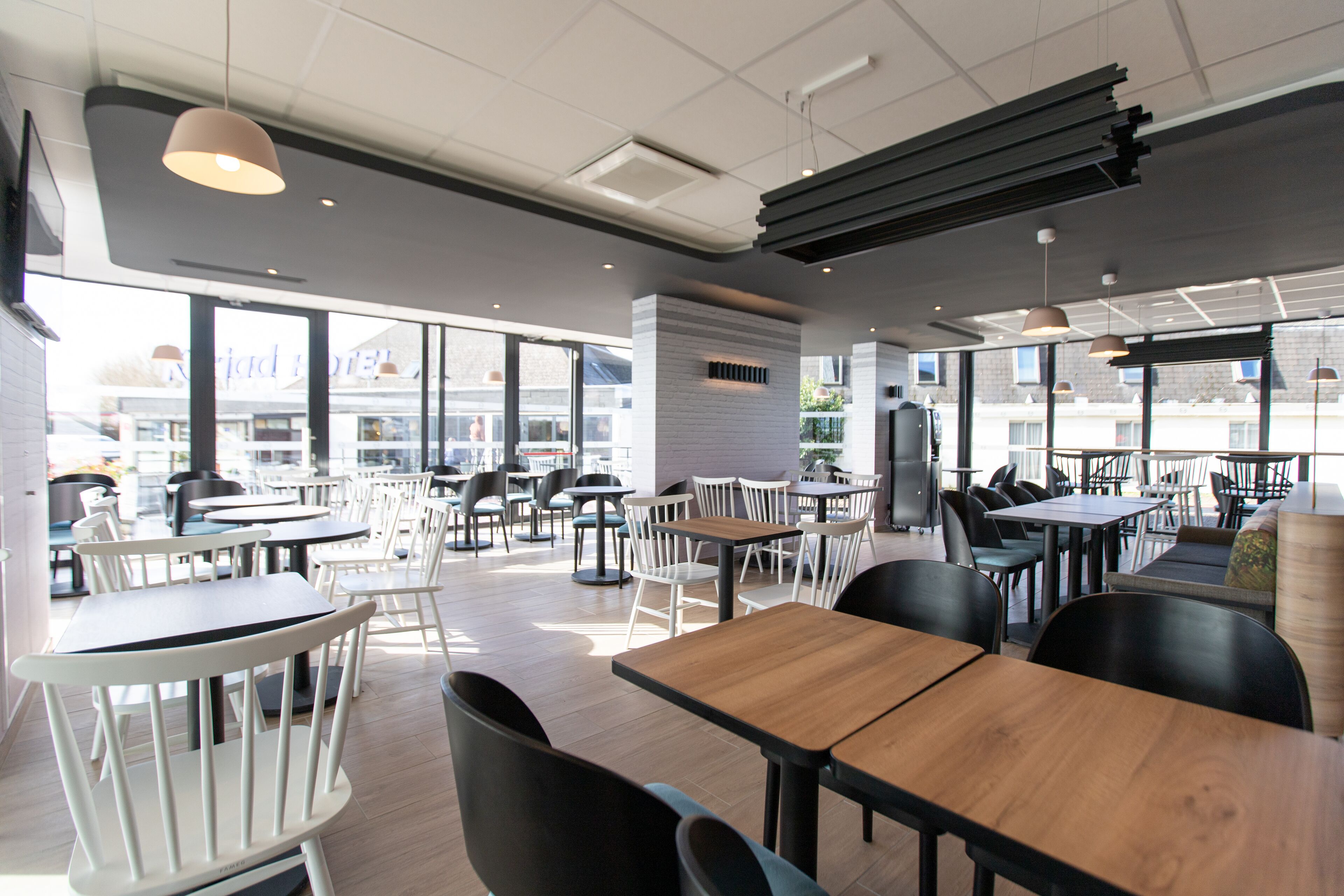 Un restaurante moderno con varias zonas de comedor, incluyendo mesas altas y cabinas, y grandes ventanales con vistas a la ciudad.