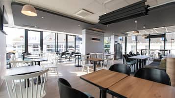 Un restaurante moderno con varias zonas de comedor, incluyendo mesas altas y cabinas, y grandes ventanales con vistas a la ciudad.