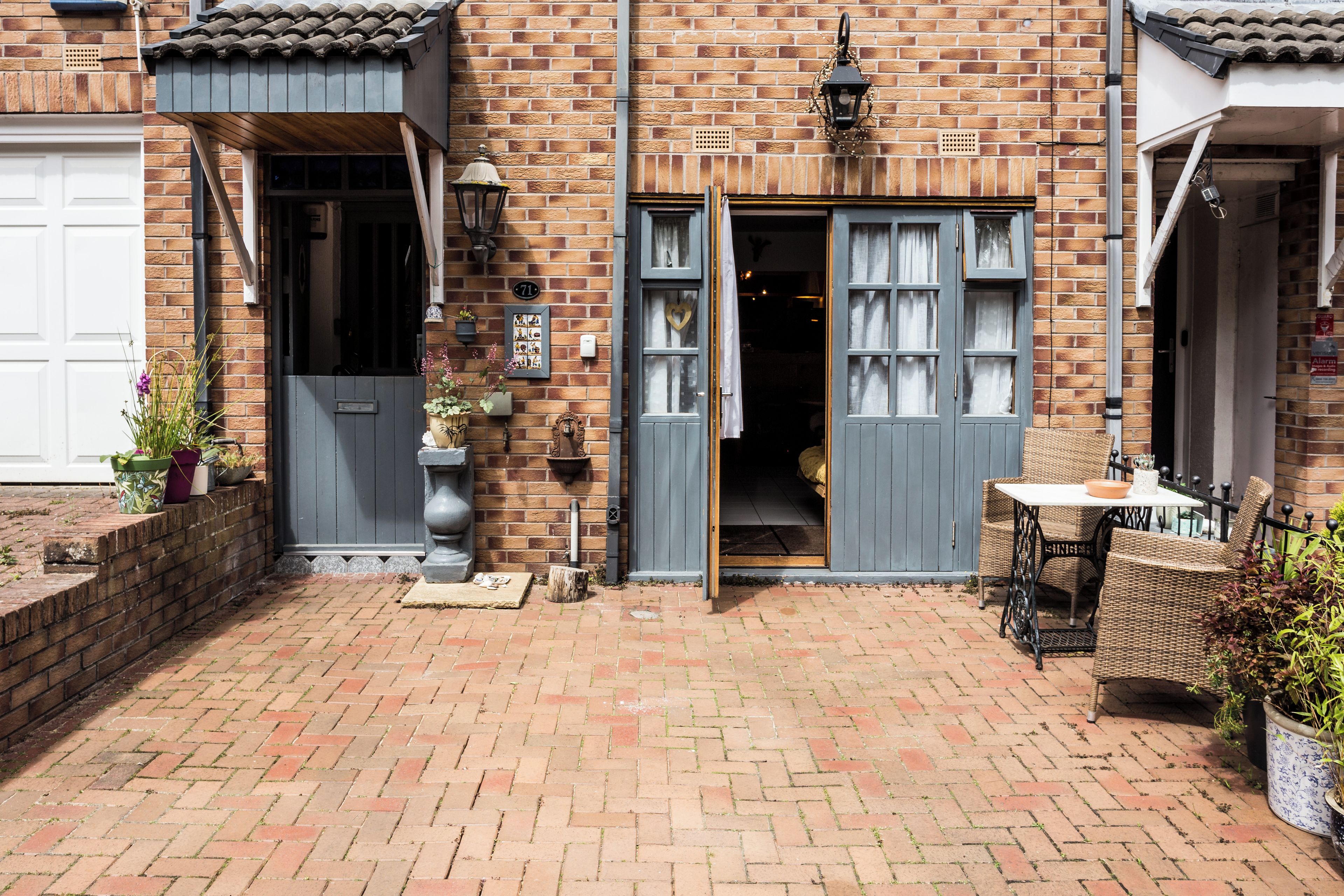 A brick building with a garage door, a door with a heart-shaped decoration, and a small outdoor seating area with a table and chairs.
