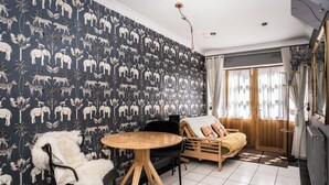 A room with a patterned wallpaper, a round wooden table, a fur-covered chair, a wooden sofa, and a window with curtains. - The Brunstane Studio  (Edinburgh, Scotland)