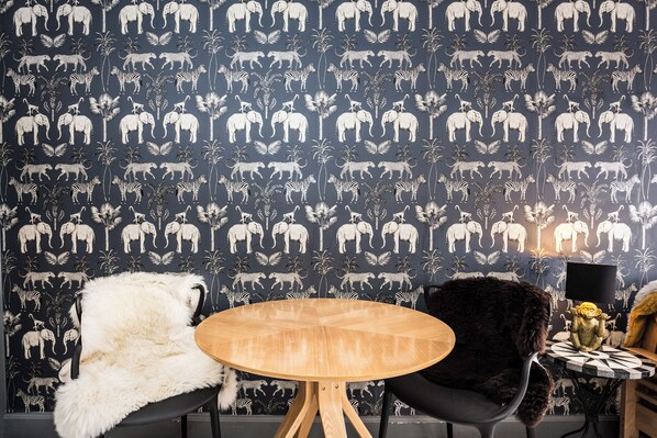 Ein Zimmer mit Wandpapier mit Tiermotiven, einem runden Holztisch und zwei Stühlen mit Fellbezug.