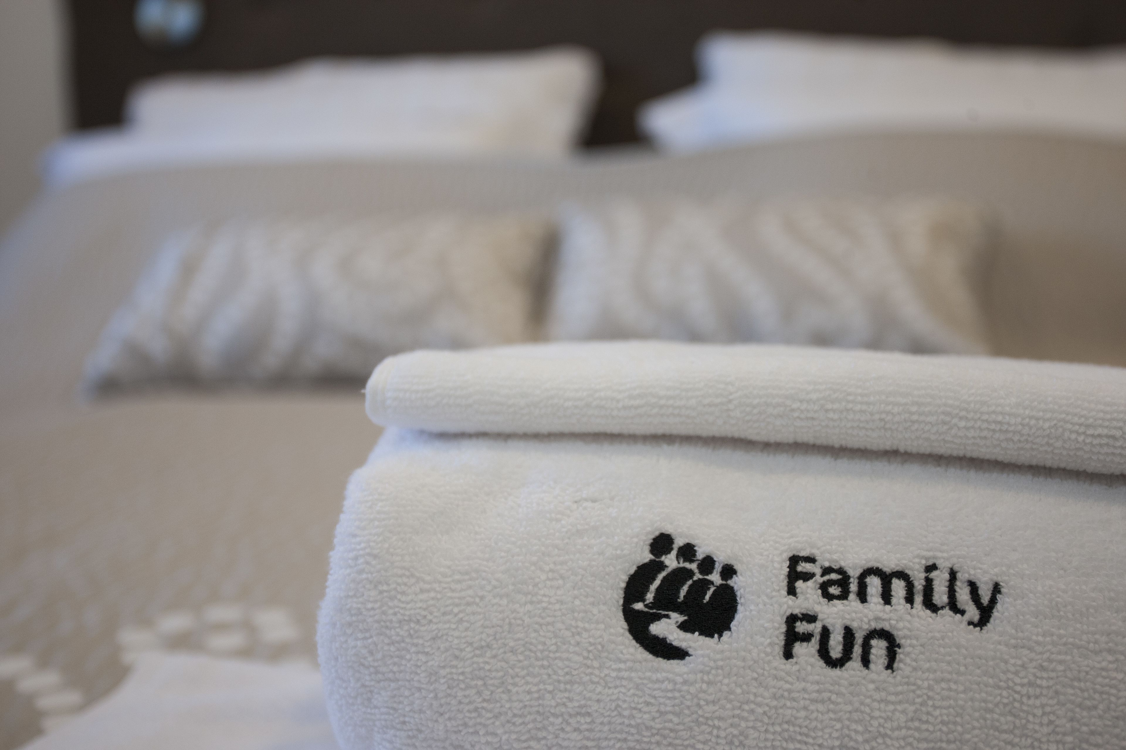 A white towel with a paw print and the words "Family Fun" on it, placed on a bed with white bedding.