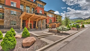 A multi-story hotel with a stone facade, a covered entrance, and a landscaped front yard with shrubs and rocks. - Large 4 Bedroom Ski-in/Out, Sleeps 12, Vaulted Ceilings, Pool, Hot Tub MC12B (Park City)
