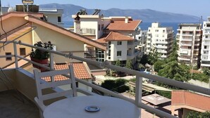Un balcon avec une table ronde et deux chaises, donnant sur un quartier résidentiel avec des immeubles et une montagne visible au loin.