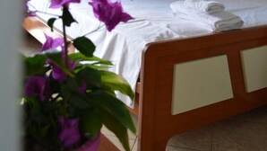 Une chambre à coucher avec un lit, du linge de lit blanc, une tête de lit en bois et une plante en pot aux fleurs violettes.