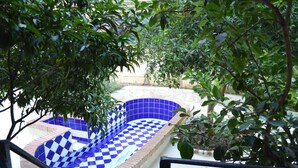 Une piscine dont le fond est recouvert de carreaux bleus et blancs, entourée de verdure.