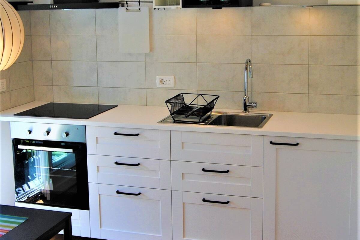 A modern kitchen with white cabinets, a black stove, and a wooden floor.