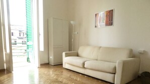 Une pièce avec un parquet en bois disposé en motif à chevrons, un canapé beige, une armoire blanche et un tableau accroché au mur.