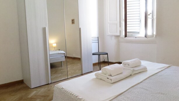 Une chambre à coucher avec un lit, une chaise, un miroir et une fenêtre avec des stores.