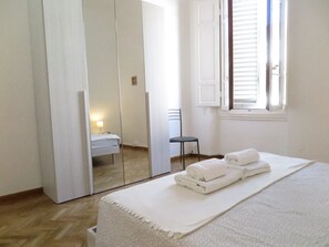 A bedroom with a bed, a chair, a mirror, and a window with blinds. - Wine Apartments Florence Merlot (Florence)
