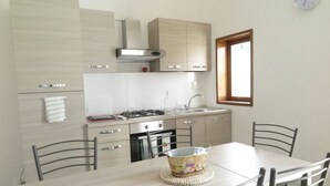 Une cuisine moderne équipée d’une cuisinière à gaz, d’un four et d’un évier. On y trouve une table à manger avec des chaises, et un vase décoratif posé sur la table.