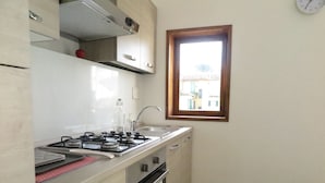 Une cuisine de taille réduite, équipée d’une cuisinière à gaz, d’un four et d’une fenêtre donnant sur les bâtiments environnants.